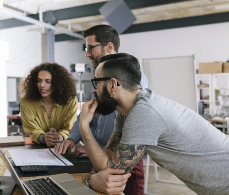 Three people working on a laptop in an office