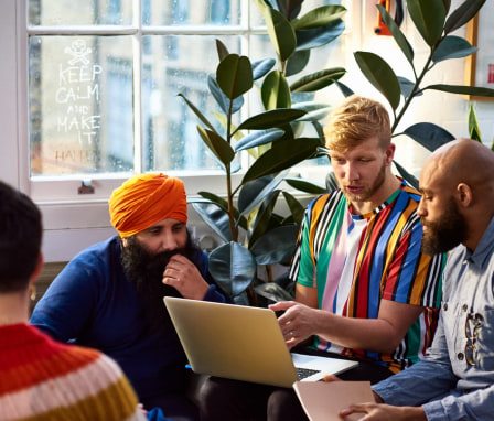 Three people talking and looking at a laptop