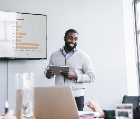 Smiling businessman holding tablet computer explaining graphs in meeting at board room