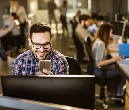 Man smiling at smartphone while working in office