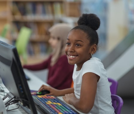 Smiling young girl typing on a computer at school