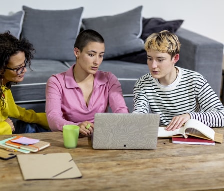 Three people working together on a laptop on a coffee table