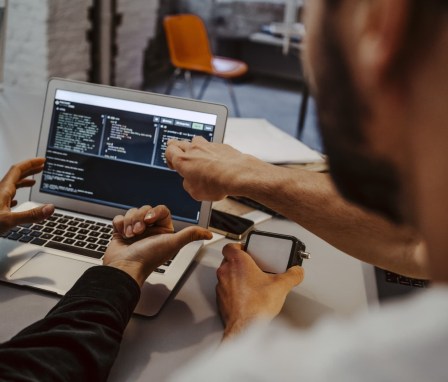 Two people coding on a laptop in an office