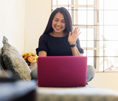 Woman waving at her laptop while sitting on a couch